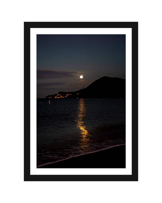Framed photograph of a moonlit night over water with a silhouette of a hill.