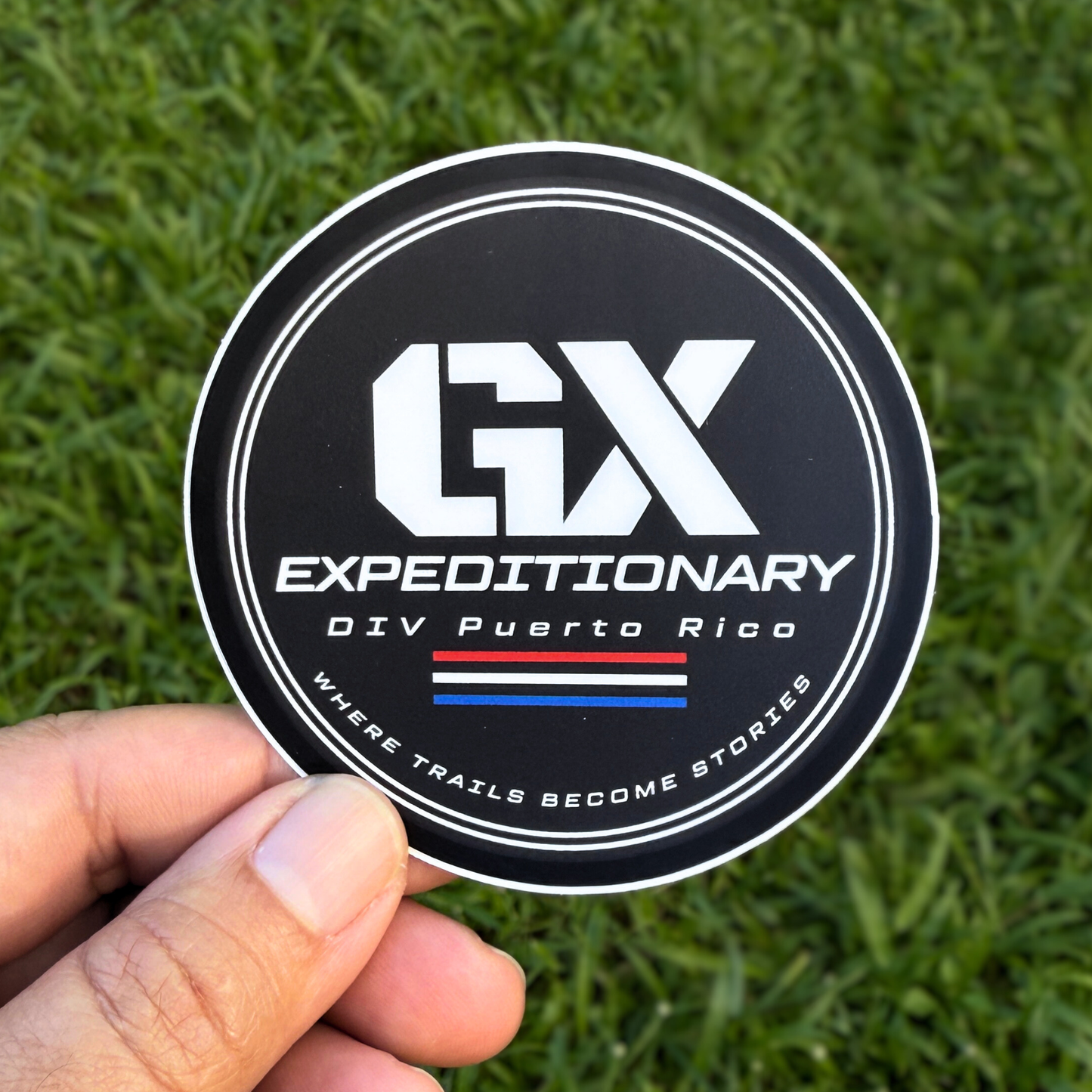 Sticker with 'GX Expeditionary' logo held over grass