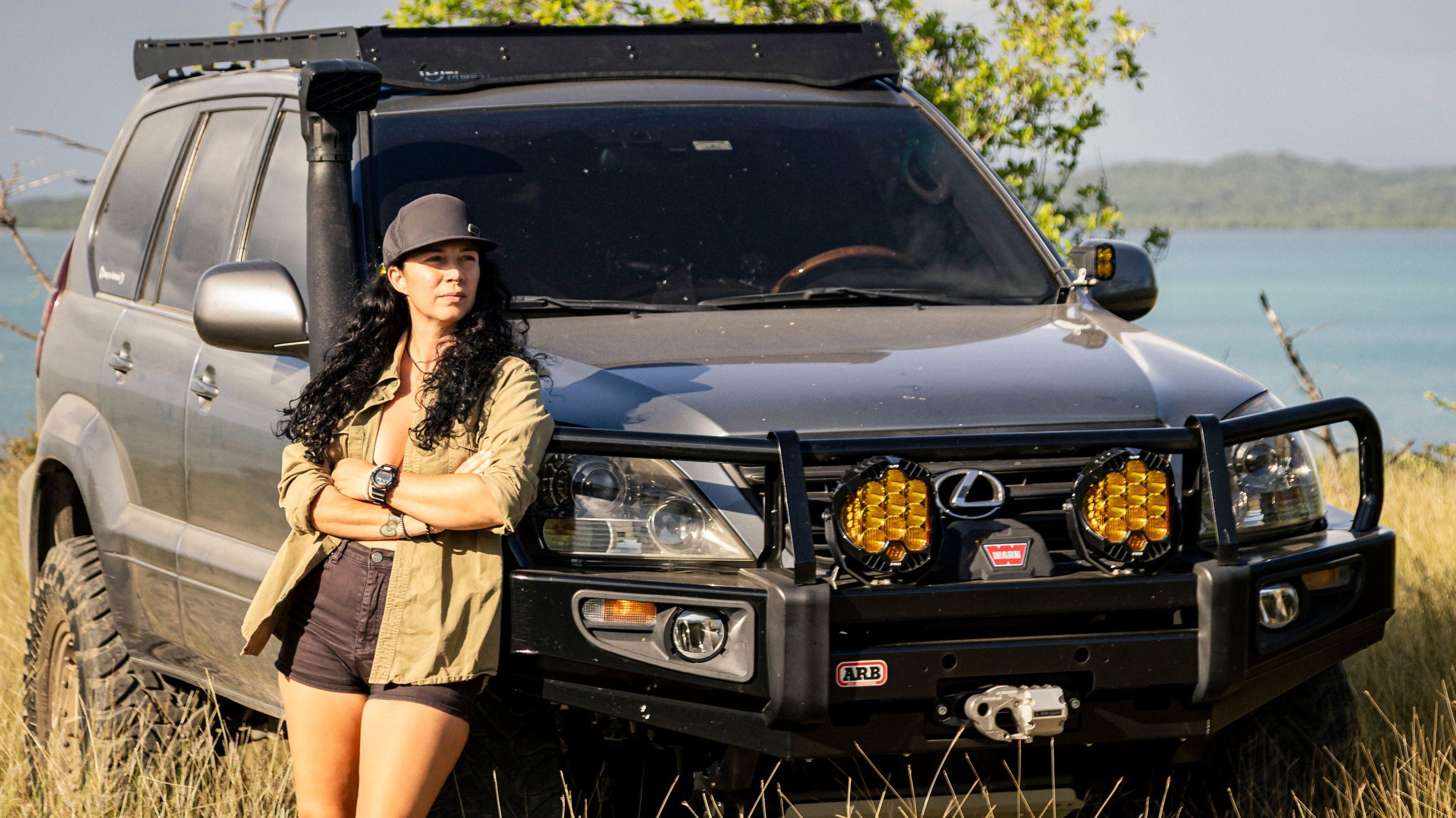 Woman standing next to a Lexus GX in a natural setting with trees and water in the background